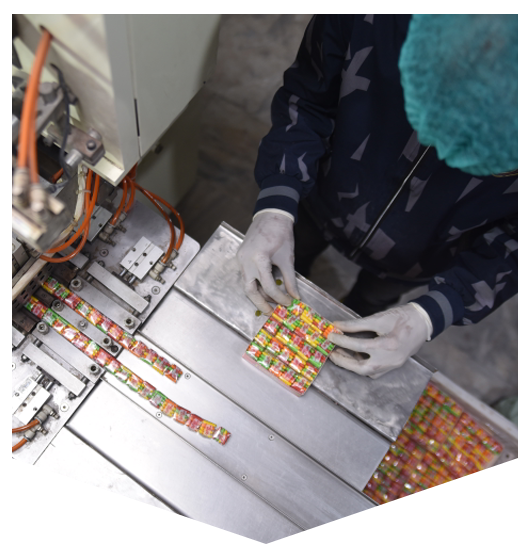 Worker arranging wrapped multi-color candies at a stainless steel station